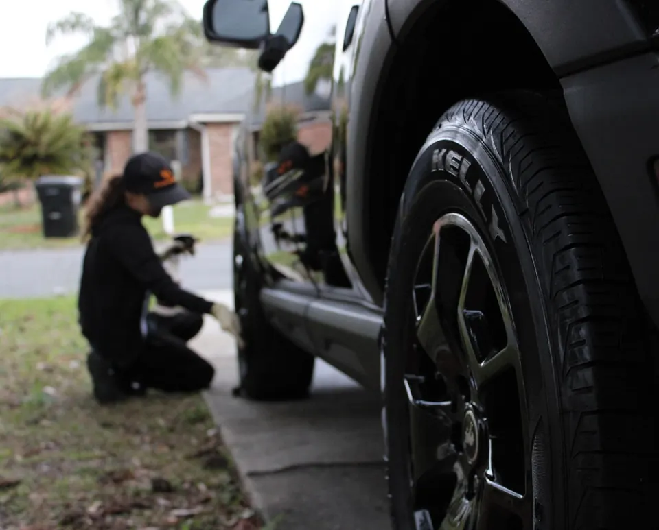 Slick Shine detailer kneeling to clean the tire of a black SUV