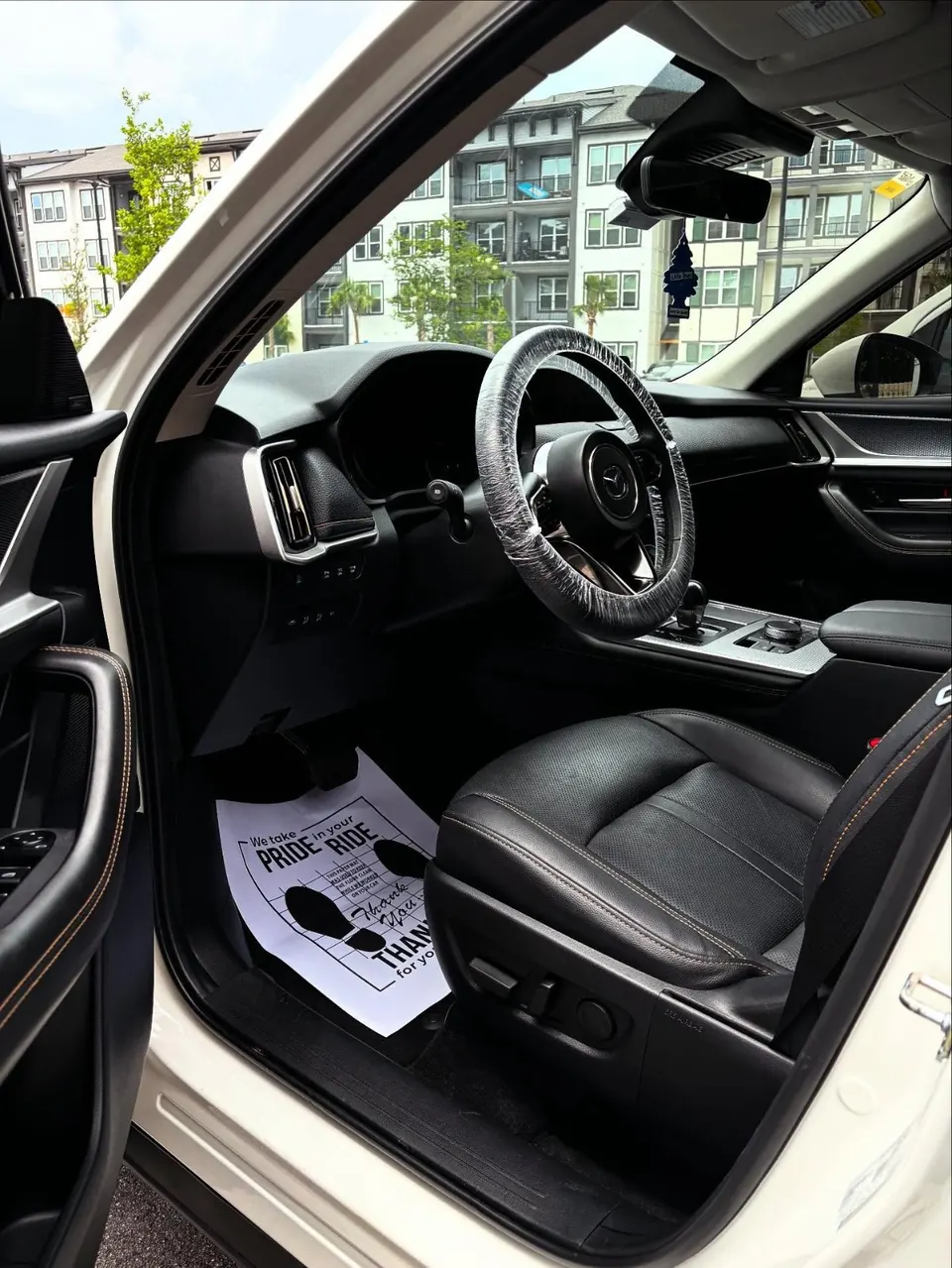 Clean black leather interior with a steering wheel cover and paper floor mat after a detail