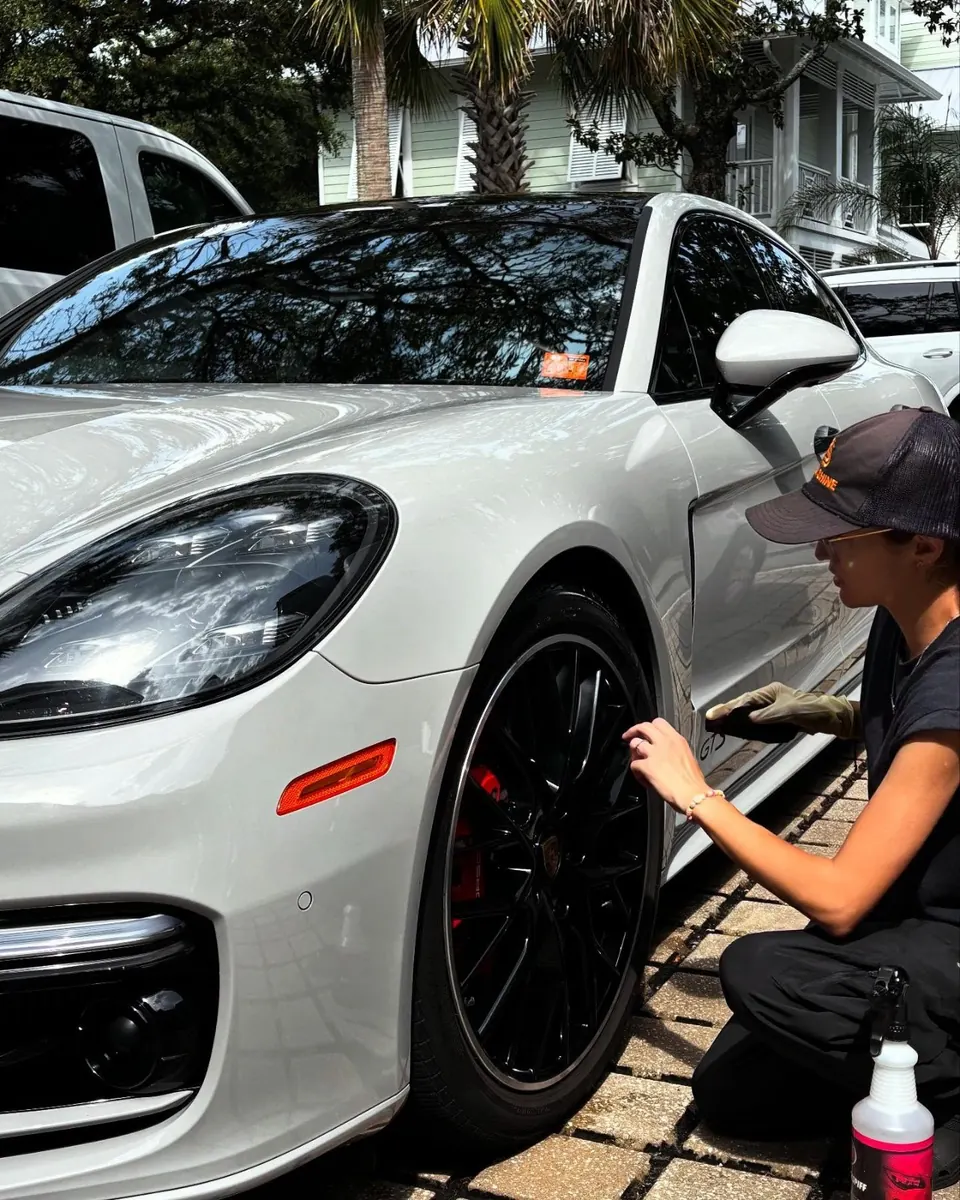 Slick Shine detailer cleaning the wheel of a white Porsche Panamera GTS during its monthly detail